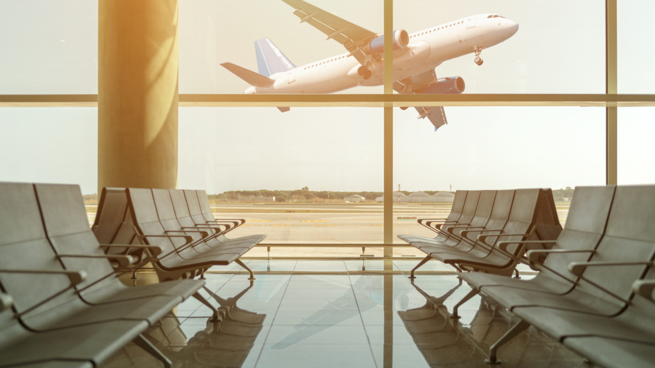 Empty chairs in the departure hall at airport on background of airplane taking off at sunset. Travel concept.